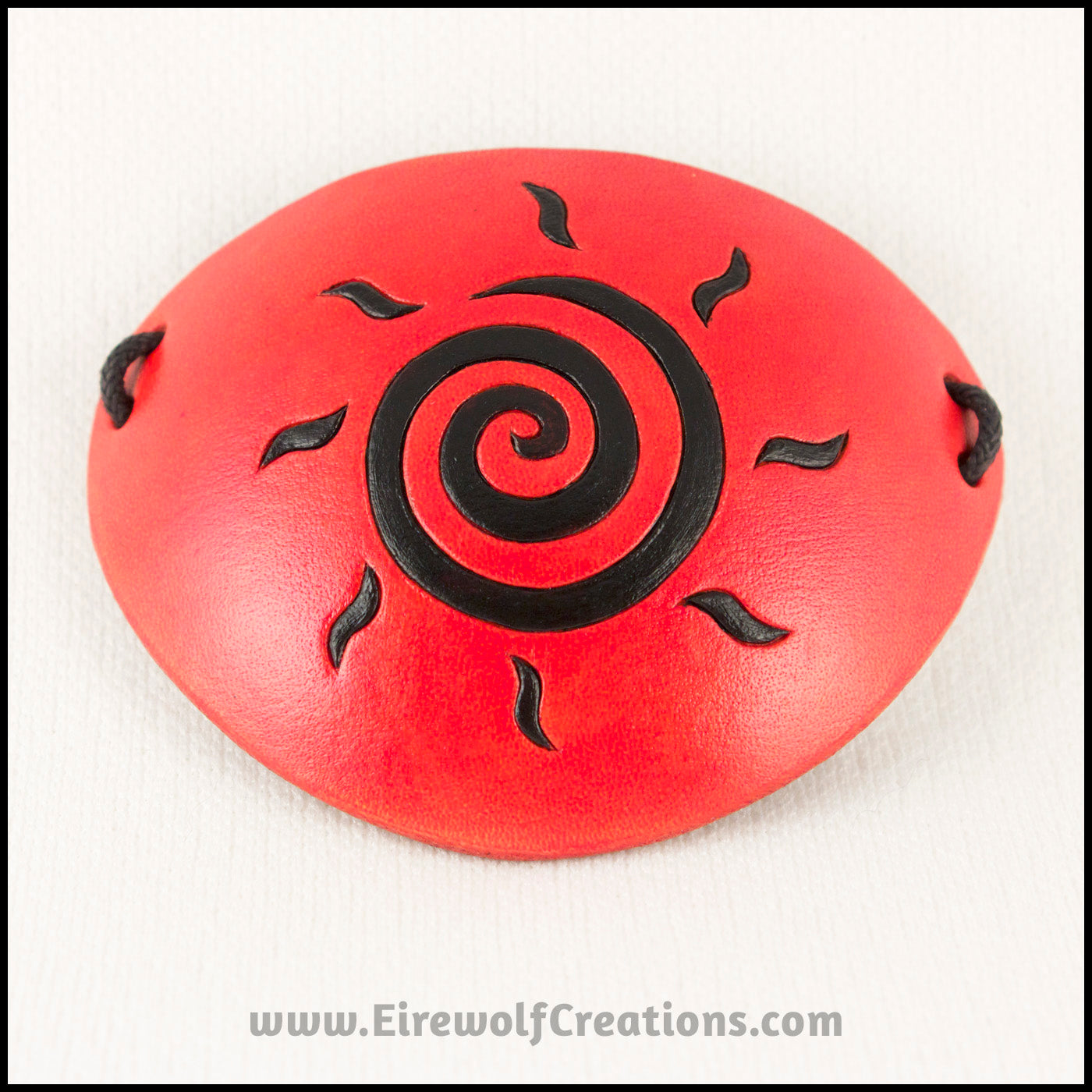 A handmade leather eye patch dyed orange with a bold black sun spiral symbol carved and painted on the leather, for a masquerade costume or pirate cosplay. By Erin Metcalf of Eirewolf Creations.