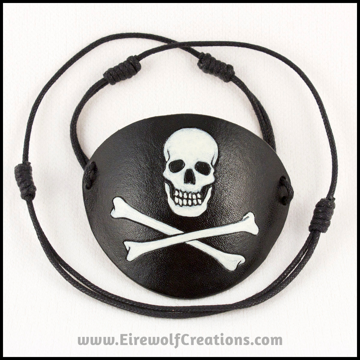 A handmade leather Jolly Roger eye patch, with hand carved and painted skull and bones, for a masquerade costume or pirate cosplay. By Erin Metcalf of Eirewolf Creations.