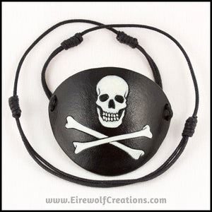 A handmade leather Jolly Roger eye patch, with hand carved and painted skull and bones, for a masquerade costume or pirate cosplay. By Erin Metcalf of Eirewolf Creations.