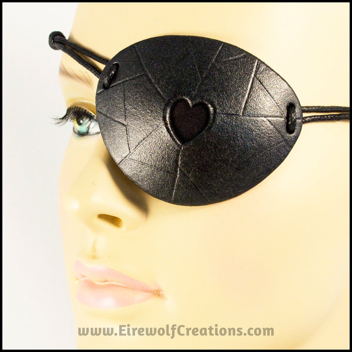 A handmade leather eye patch with a heart cut out, subtly iridescent black, backed with transparent black fabric to allow some visibility, for a masquerade costume or pirate cosplay. By Erin Metcalf of Eirewolf Creations.
