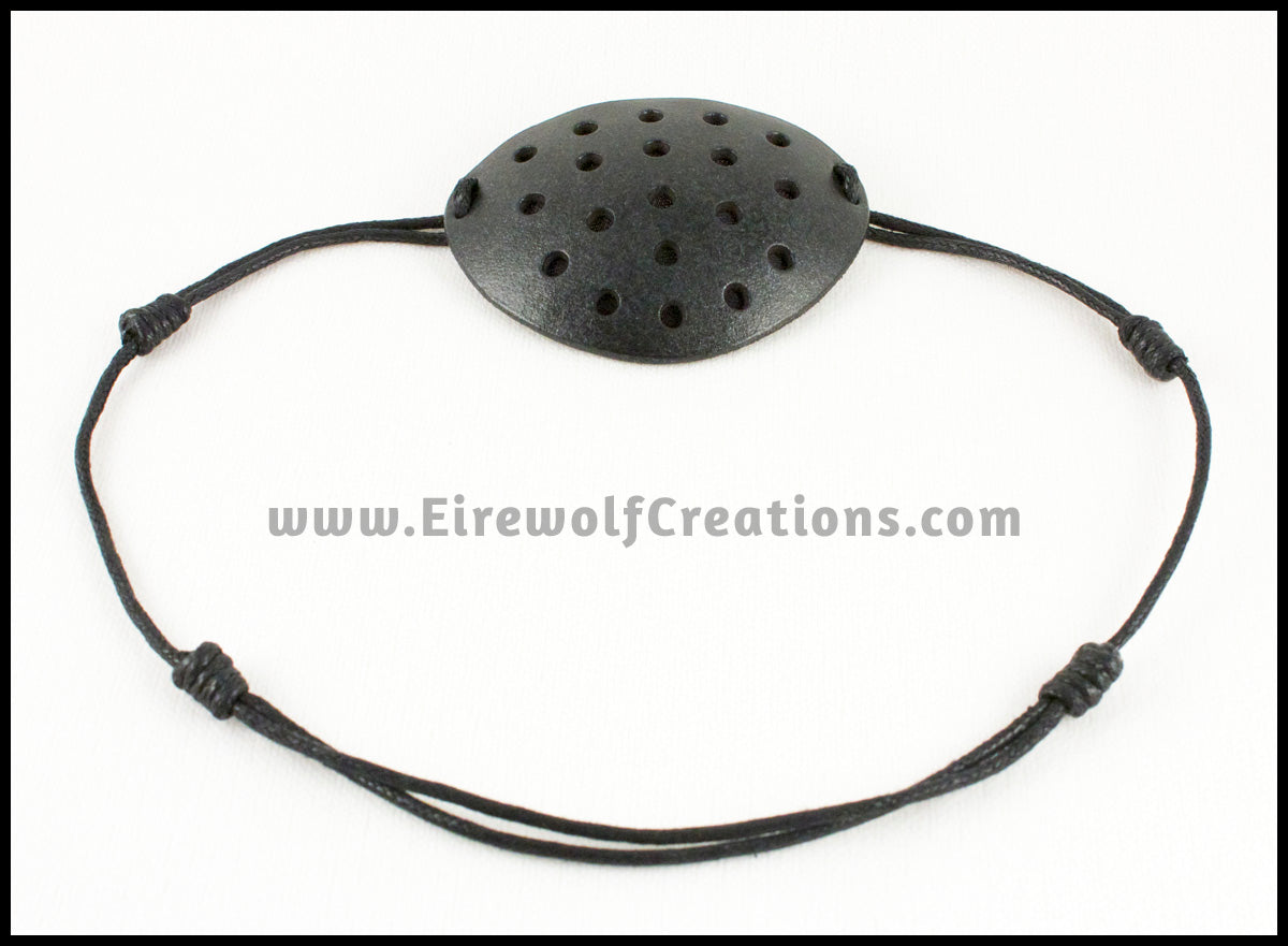 A handmade leather industrial style costume eye patch with 19 holes punched in it to allow some visibility, painted subtly sparkly black and backed with transparent black fabric. By Erin Metcalf of Eirewolf Creations.