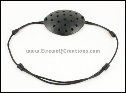 A handmade leather industrial style costume eye patch with 19 holes punched in it to allow some visibility, painted subtly sparkly black and backed with transparent black fabric. By Erin Metcalf of Eirewolf Creations.