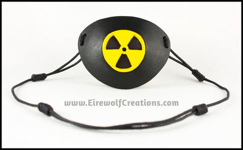 A handmade leather masquerade costume eye patch with a radiation hazard symbol cut out of the leather, painted black and bright yellow and backed with transparent black fabric to allow some visibility. By Erin Metcalf of Eirewolf Creations.