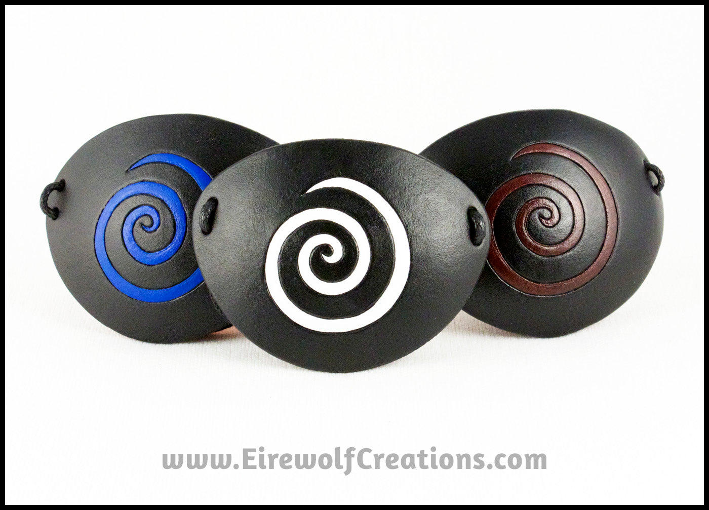 A thin spiral carved and painted cobalt blue, white, or dark red onto a handmade black leather eye patch, for a masquerade costume or pirate cosplay. By Erin Metcalf of Eirewolf Creations.