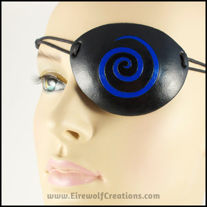 A handmade black leather eye patch with a carved and painted cobalt blue spiral, for a masquerade costume or pirate cosplay. By Erin Metcalf of Eirewolf Creations.