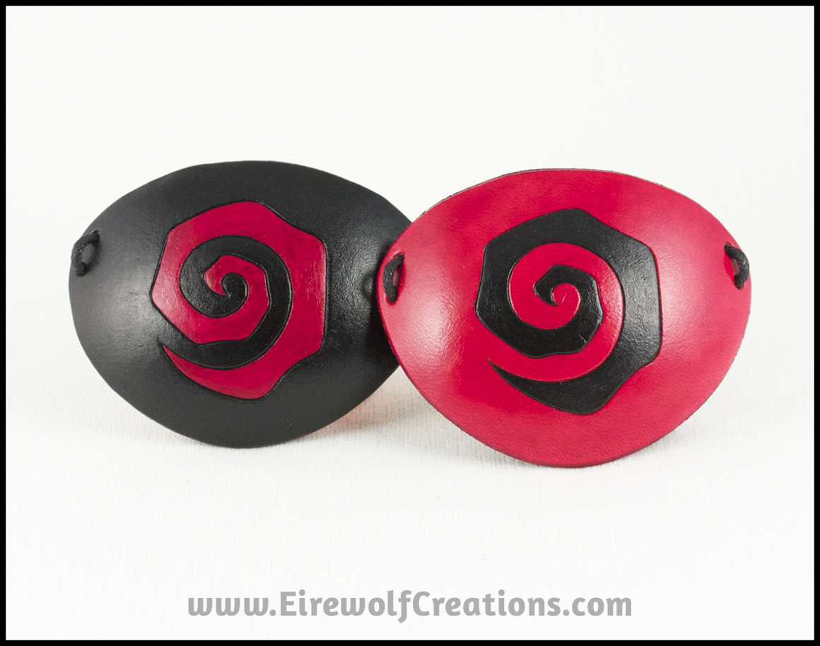 Handmade leather eye patches with a chunky Burtonesque spiral carved and painted red and black, for a masquerade costume or pirate cosplay. By Erin Metcalf of Eirewolf Creations.