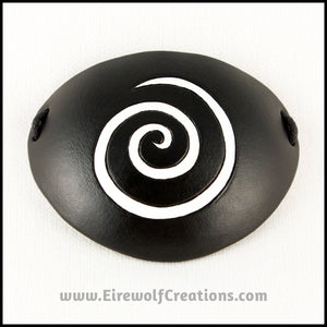 A thin spiral carved and painted white onto a handmade black leather eye patch, for a masquerade costume or pirate cosplay. By Erin Metcalf of Eirewolf Creations.