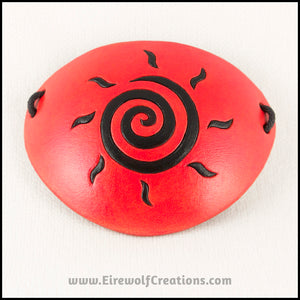 A handmade leather eye patch dyed orange with a bold black sun spiral symbol carved and painted on the leather, for a masquerade costume or pirate cosplay. By Erin Metcalf of Eirewolf Creations.