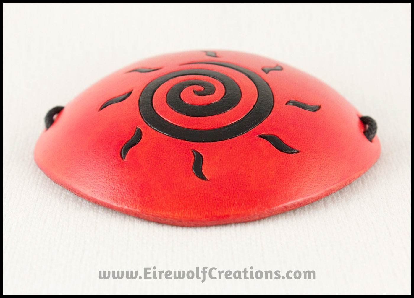 A handmade leather eye patch dyed orange with a bold black sun spiral symbol carved and painted on the leather, for a masquerade costume or pirate cosplay. By Erin Metcalf of Eirewolf Creations.