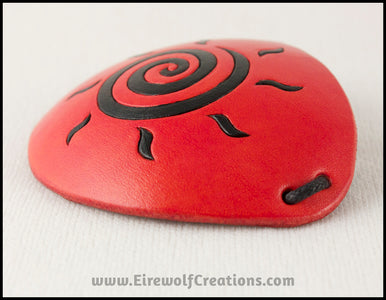 A handmade leather eye patch dyed orange with a bold black sun spiral symbol carved and painted on the leather, for a masquerade costume or pirate cosplay. By Erin Metcalf of Eirewolf Creations.