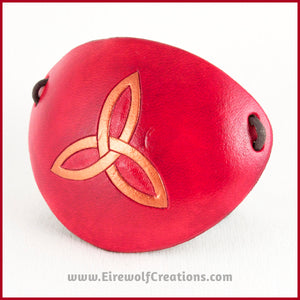 A handmade leather eye patch with a triquetra, or Celtic trinity knot, carved and painted copper on a dyed red background, for a masquerade costume or pirate cosplay. By Erin Metcalf of Eirewolf Creations.