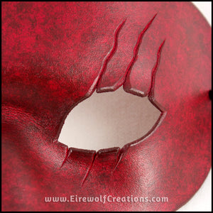 Detail of a handmade leather mask with 3 scars slashing across one eye, dyed and painted a mottled red reminiscent of blood. By Erin Metcalf of Eirewolf Creations.
